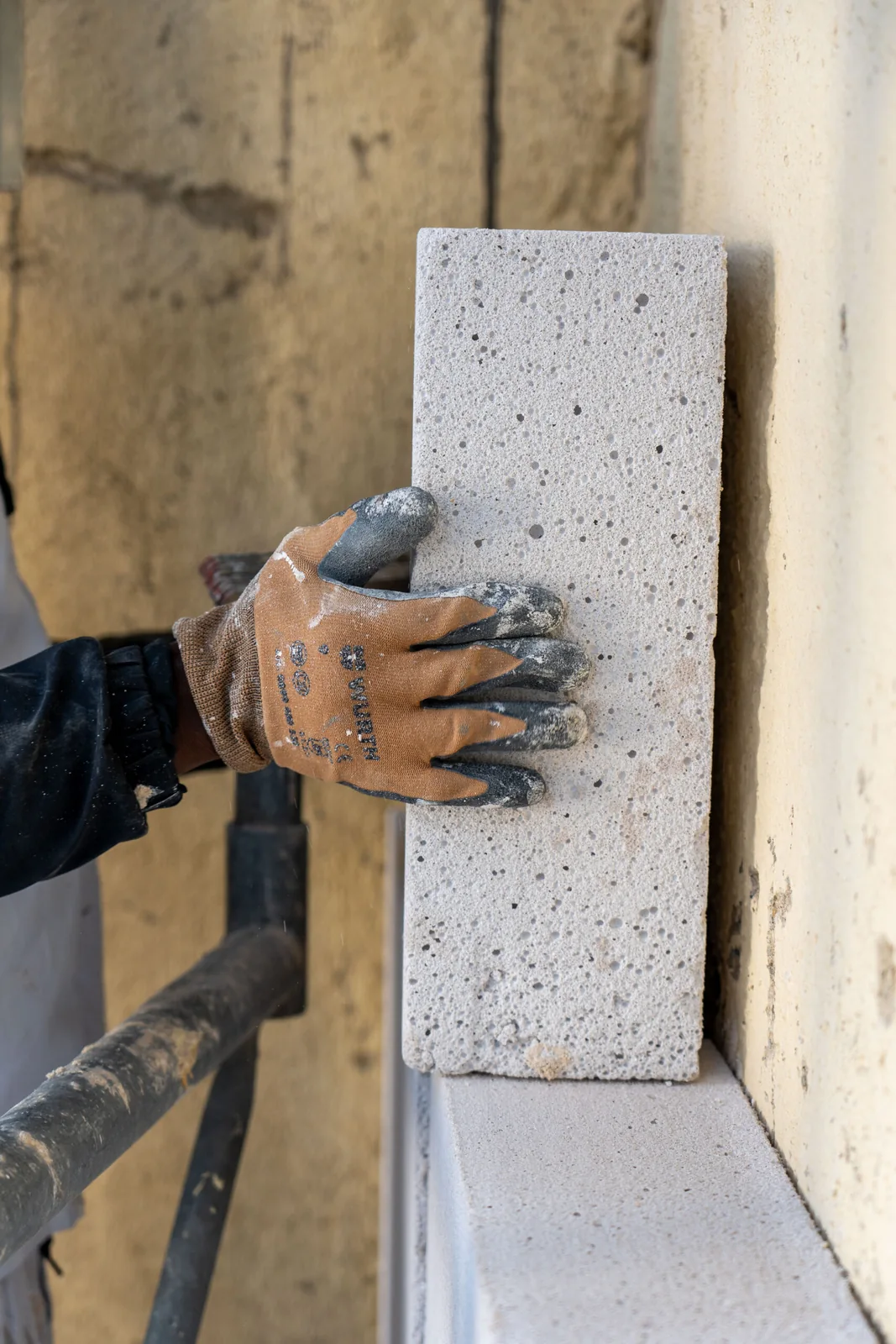 Main gantée maintenant un panneau isolant le long d’un mur de façade