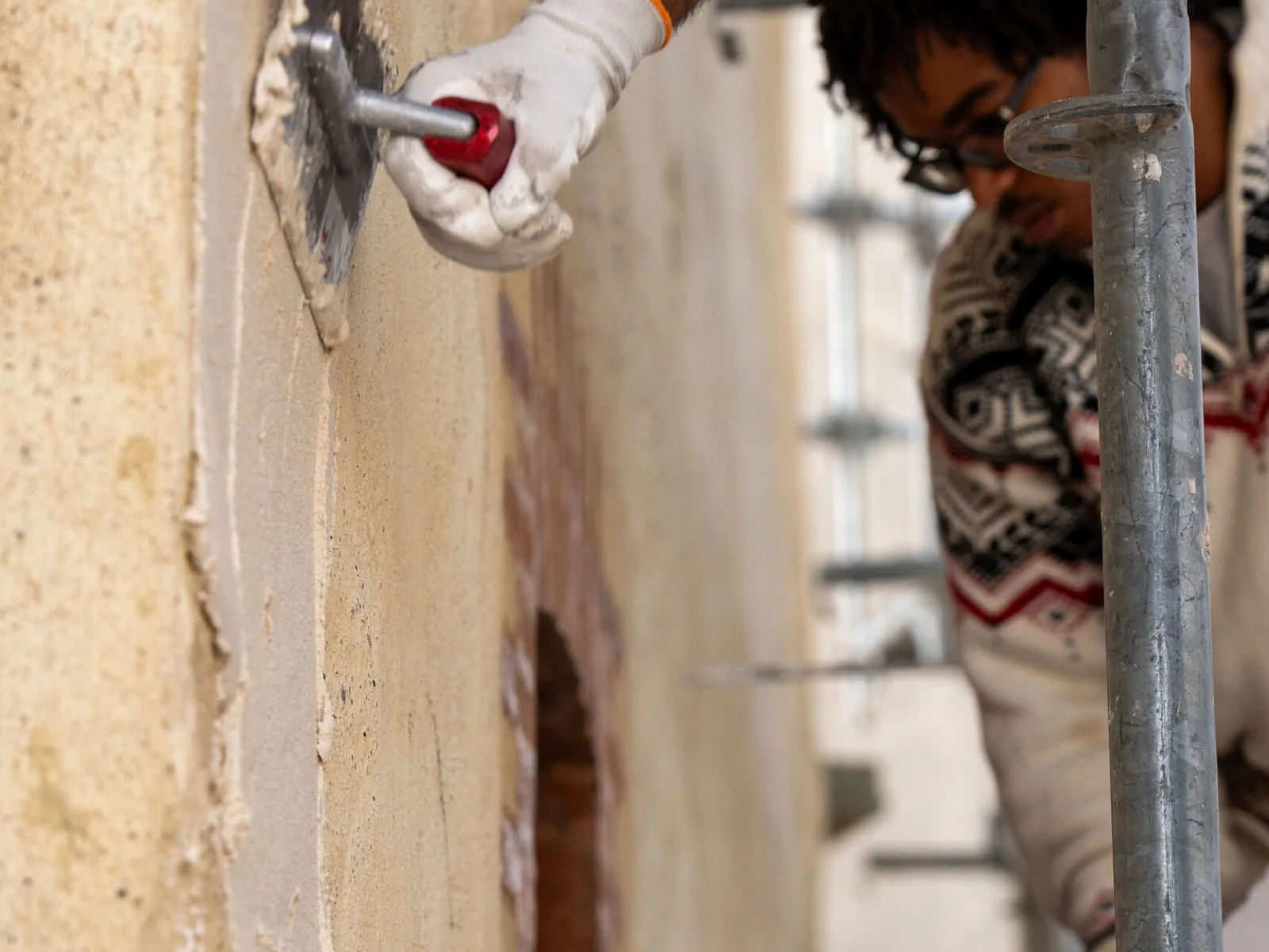 Main gantée appliquant du mortier sur un mur de façade en rénovation
