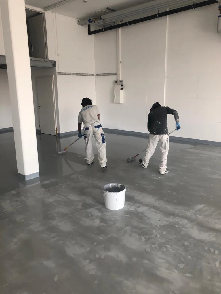 Deux artisans appliquant un revêtement de sol dans un espace intérieur en chantier